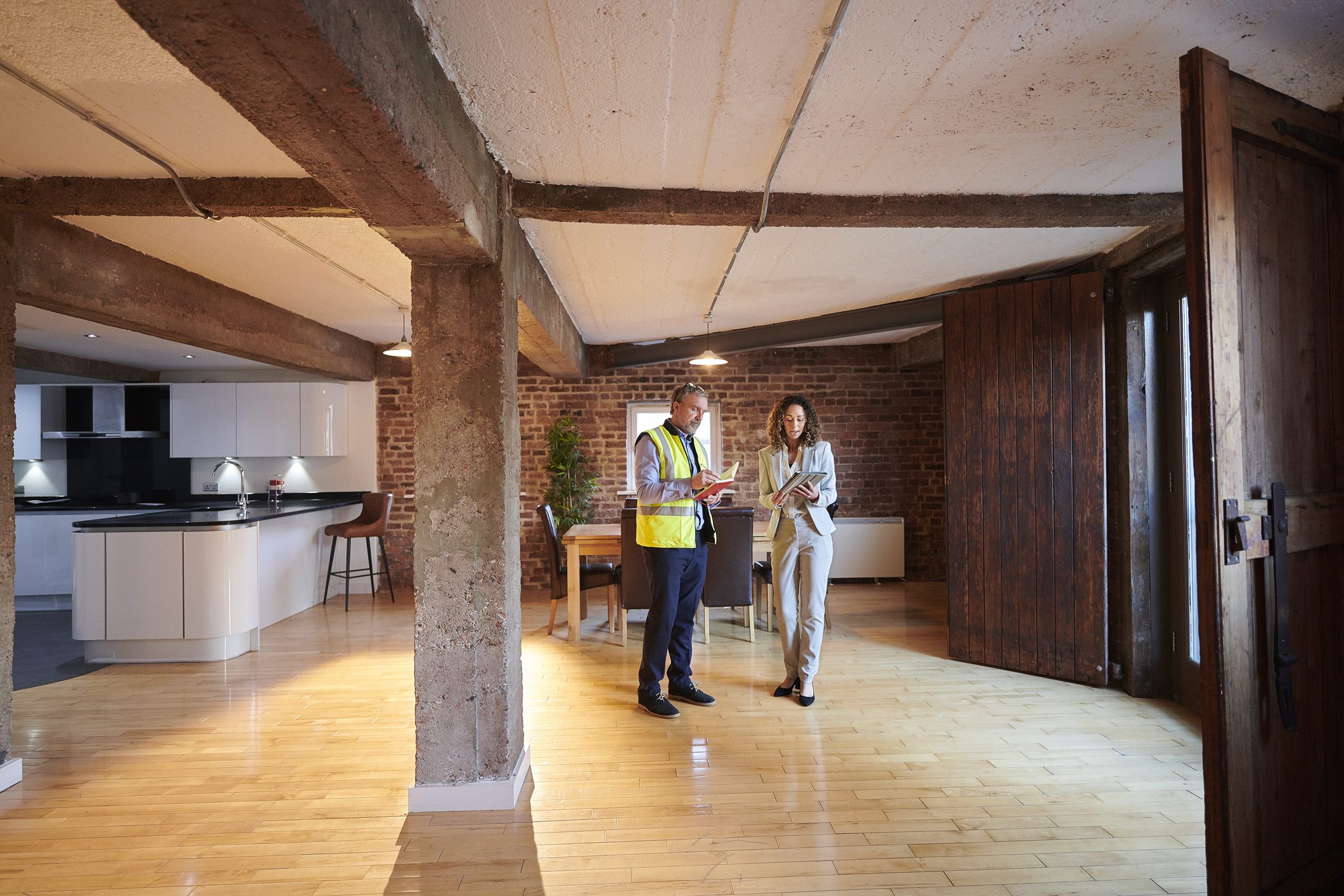 Two people discussing inside an empty room with wooden floors and beams.