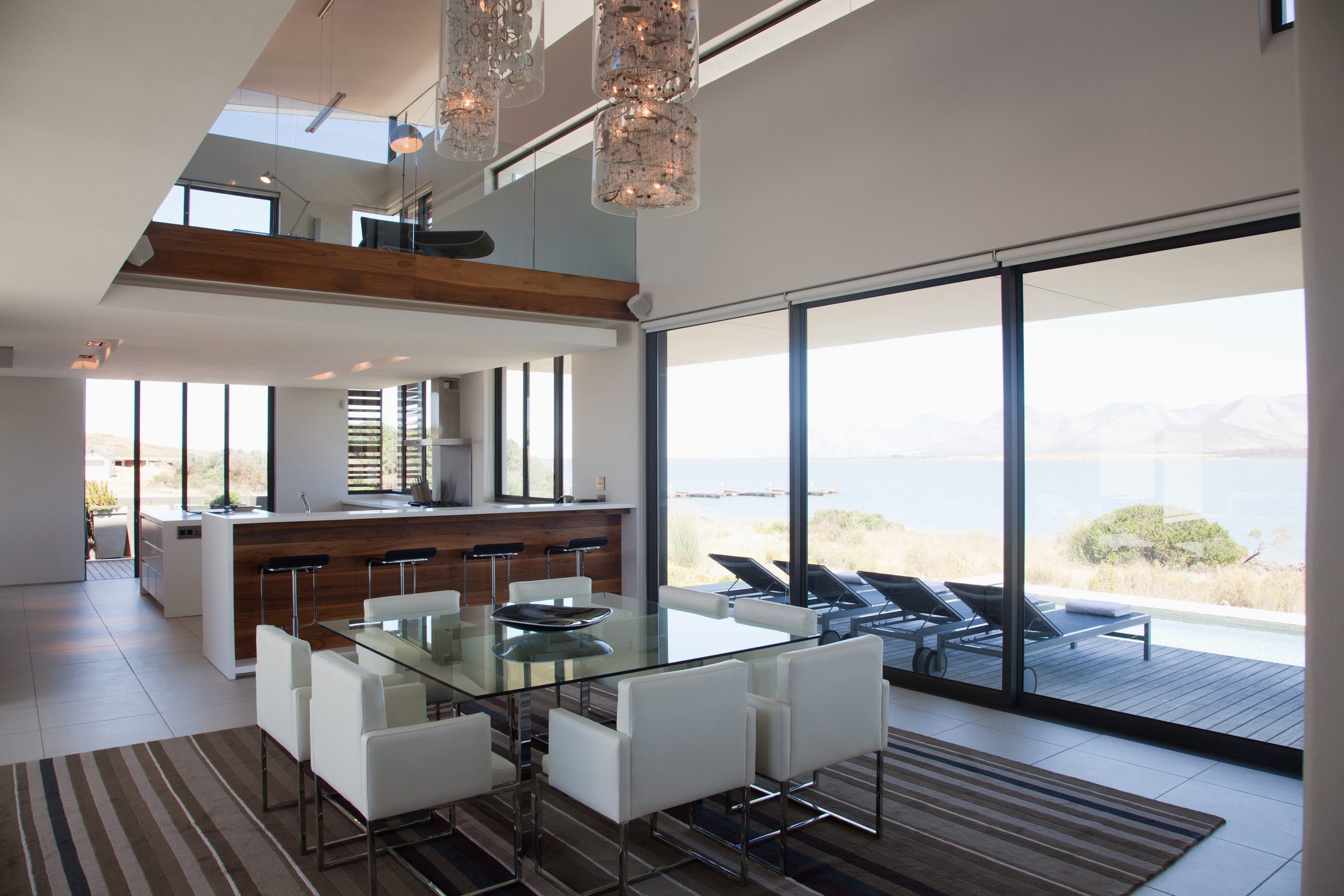 Modern dining area with glass table and ocean view windows.