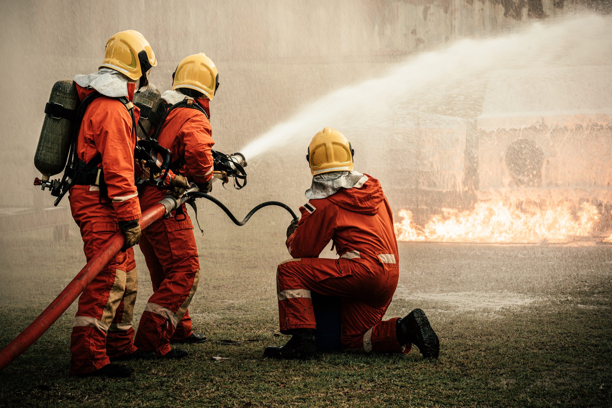 Firefighters in protective gear extinguishing a fire with a hose.