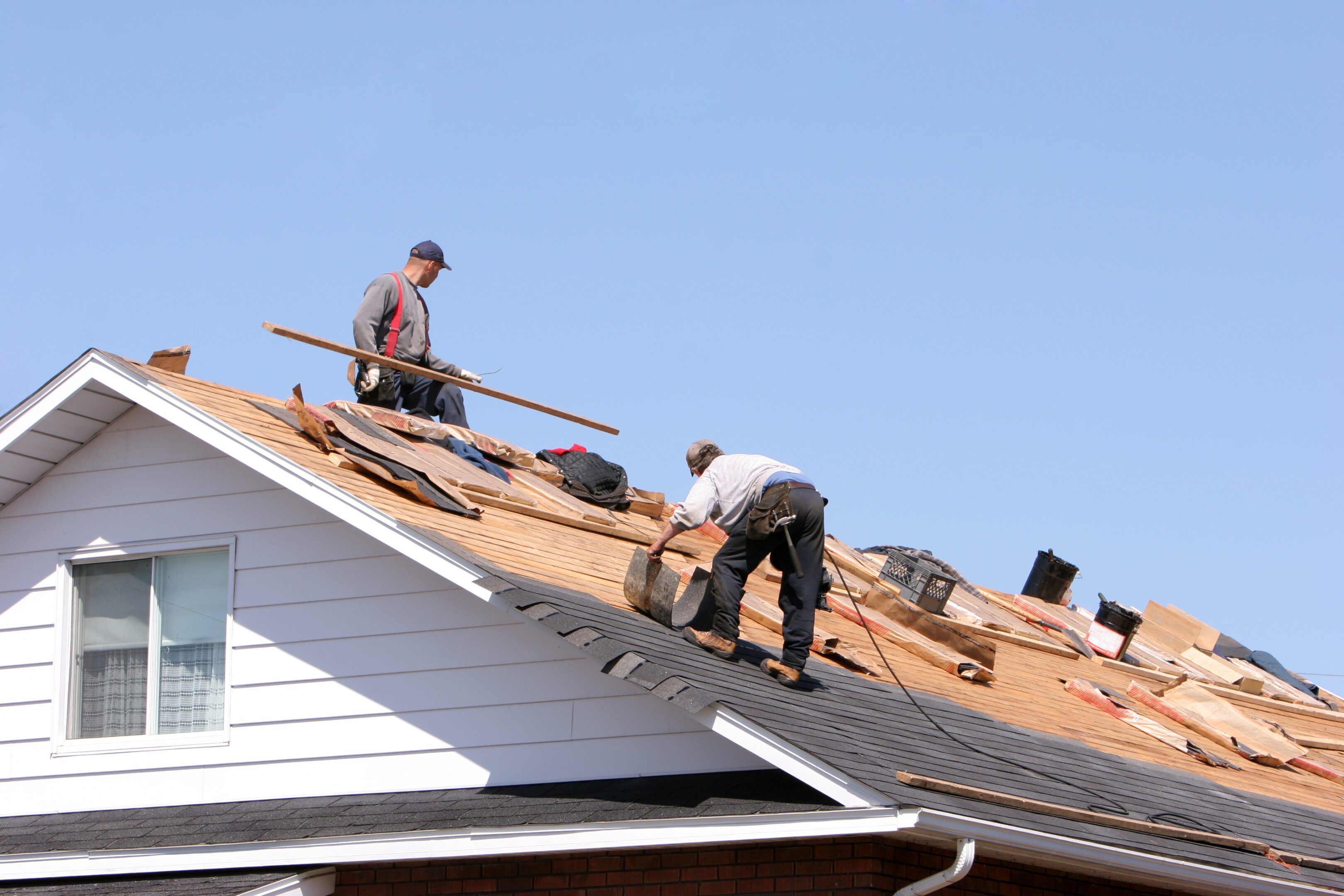 Two workers repairing a roof on a clear day.