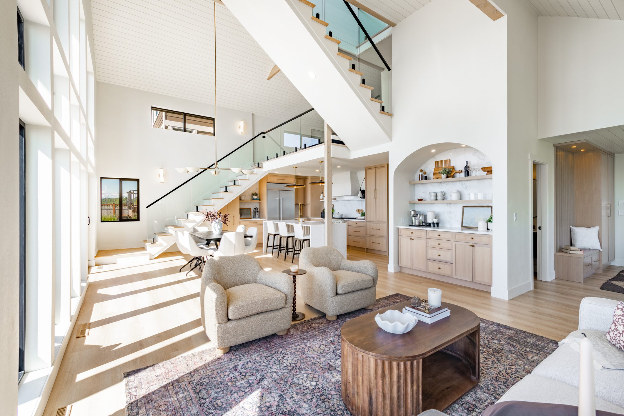 Bright modern living room with beige sofas and glass staircase.