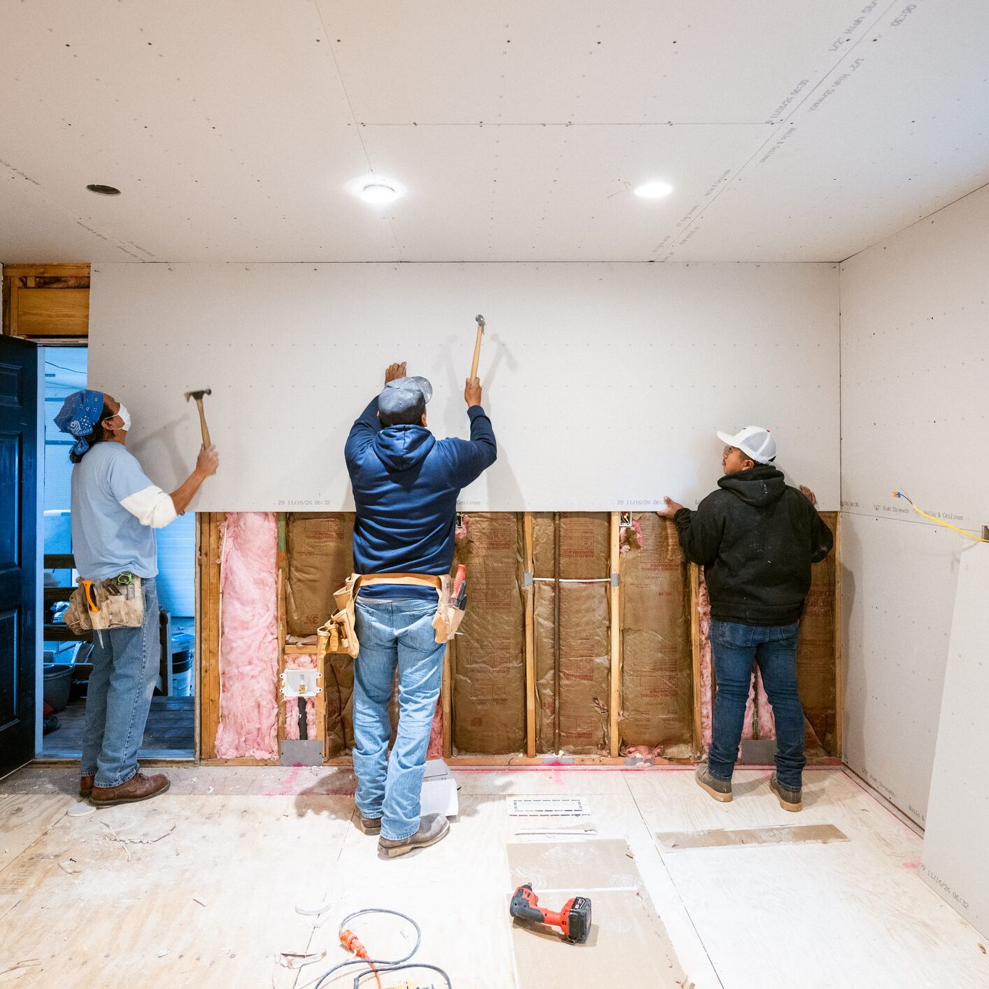 Three men renovating a room by removing wall panels.