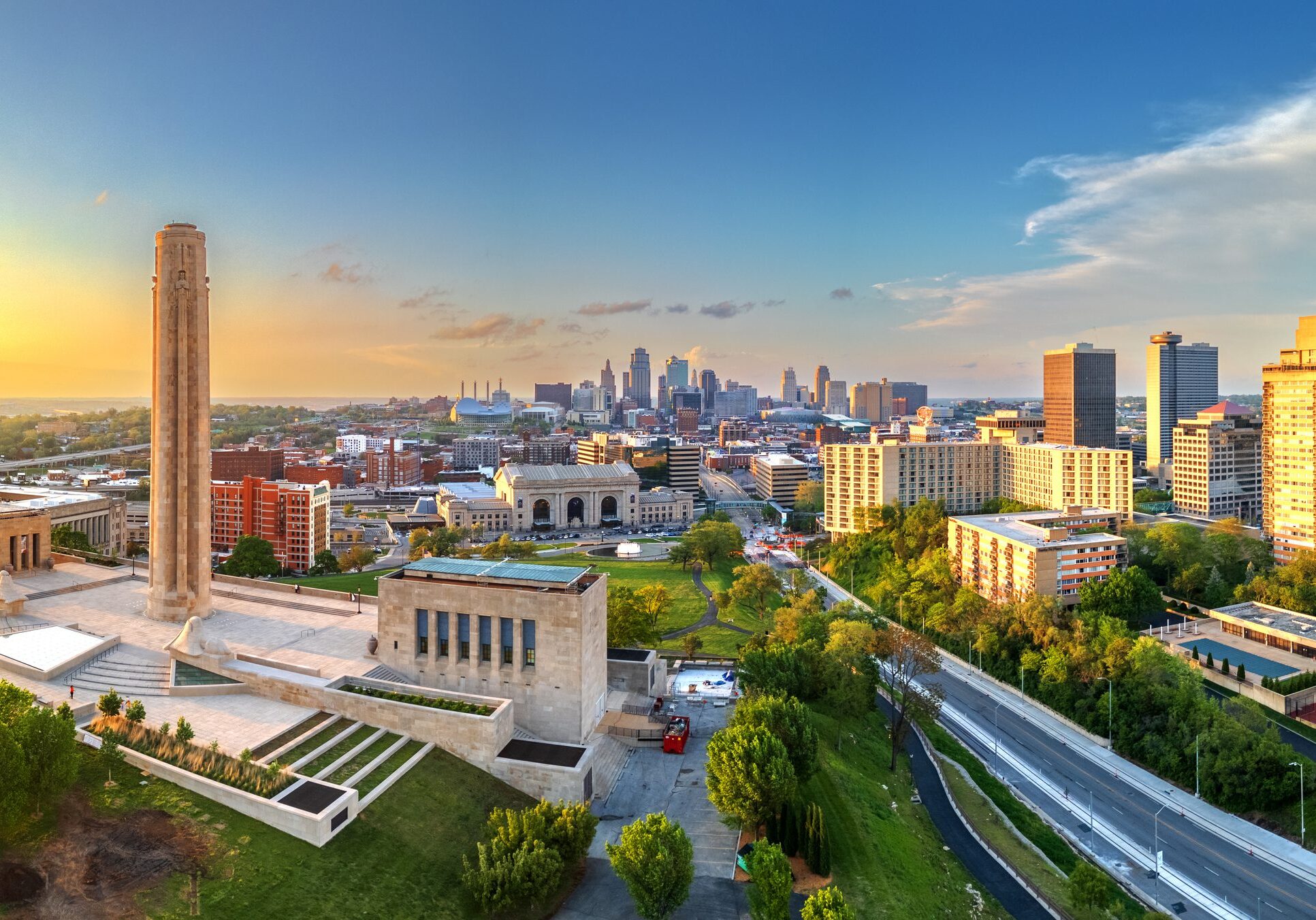 City skyline at sunset with vibrant sky and lush greenery.
