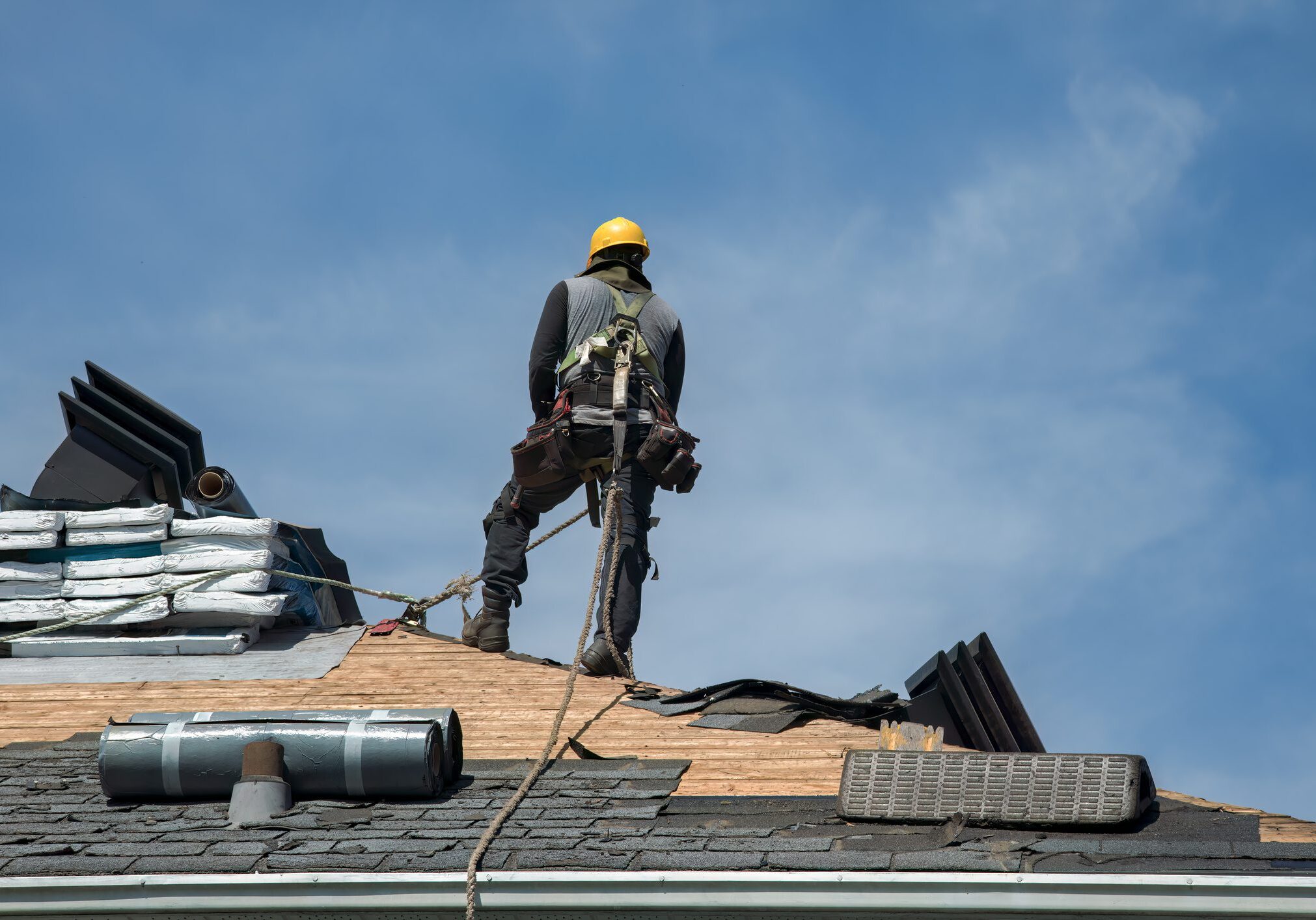 Construction worker standing on a roof under a clear sky.