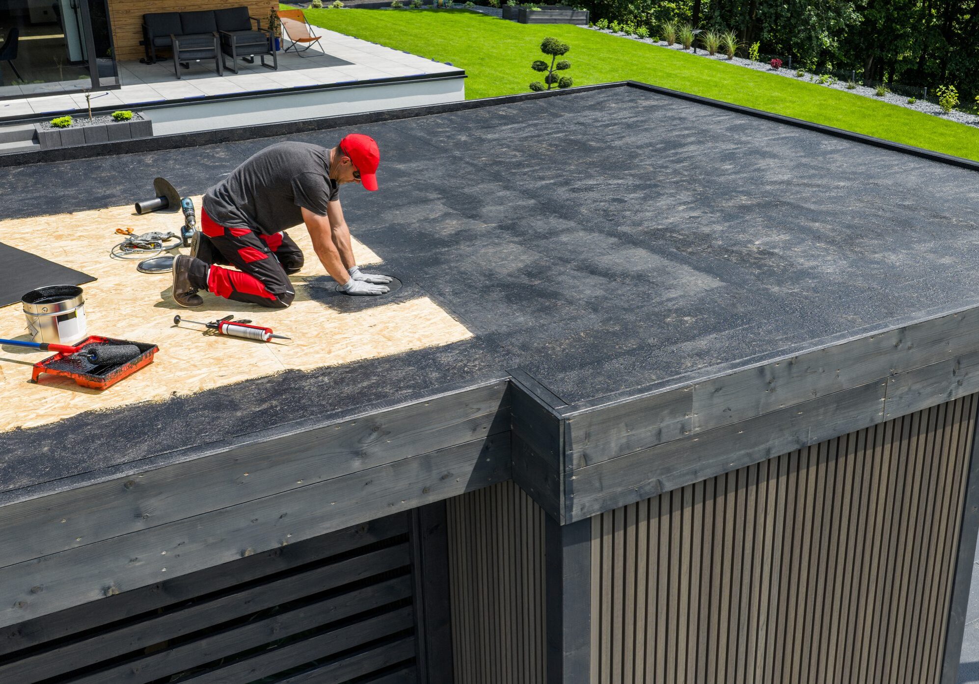 Worker installing black tiles on a roof under sunny conditions.