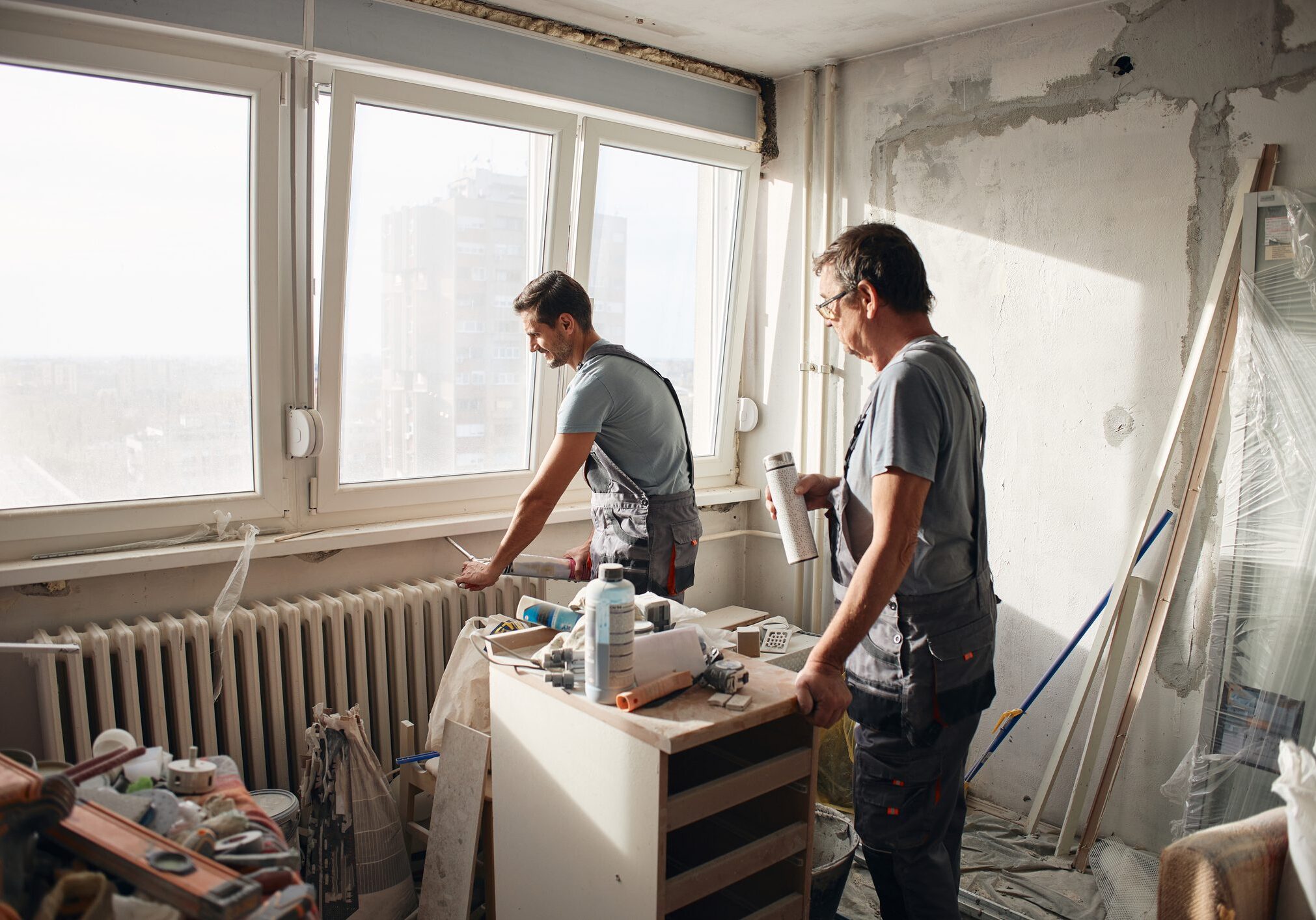 Two men renovating a room with tools and paint supplies.